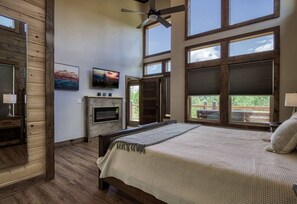 A bedroom with a large bed, a ceiling fan, a fireplace, and large windows. - Brand New Modern Mountain Chalet (Gatlinburg)