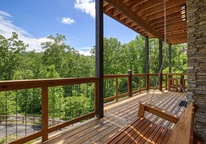 A wooden deck with a bench, stone wall, and a view of a forest.