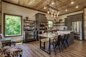 A spacious kitchen with a wooden ceiling, a dining area with a table and chairs, and a large window providing a view of the outdoors. - Brand New Modern Mountain Chalet (Gatlinburg)