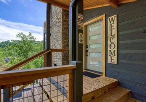 A wooden staircase leading to a door with a 'WELCOME' sign, a stone wall, and a view of a forested area. - Brand New Modern Mountain Chalet (Gatlinburg)