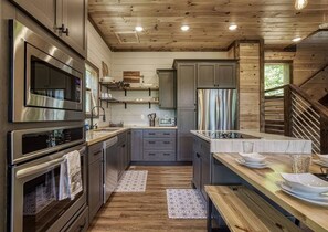 A modern kitchen with stainless steel appliances, wooden flooring, and a built-in island with a sink.