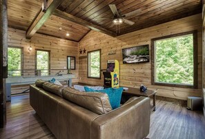 A cabin interior with a wooden ceiling, a leather sofa, a small table, and a large window. - Brand New Modern Mountain Chalet (Gatlinburg)