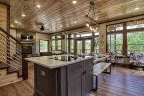 A spacious kitchen with a large island, wooden flooring, and a stone fireplace. - Brand New Modern Mountain Chalet (Gatlinburg)