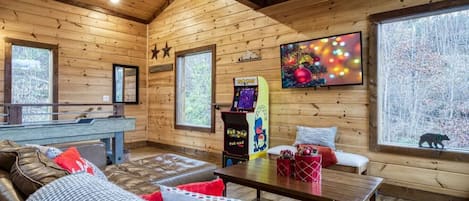 Un interior de cabaña acogedor, con paredes de madera, un sofá, una mesa y una consola de juegos.