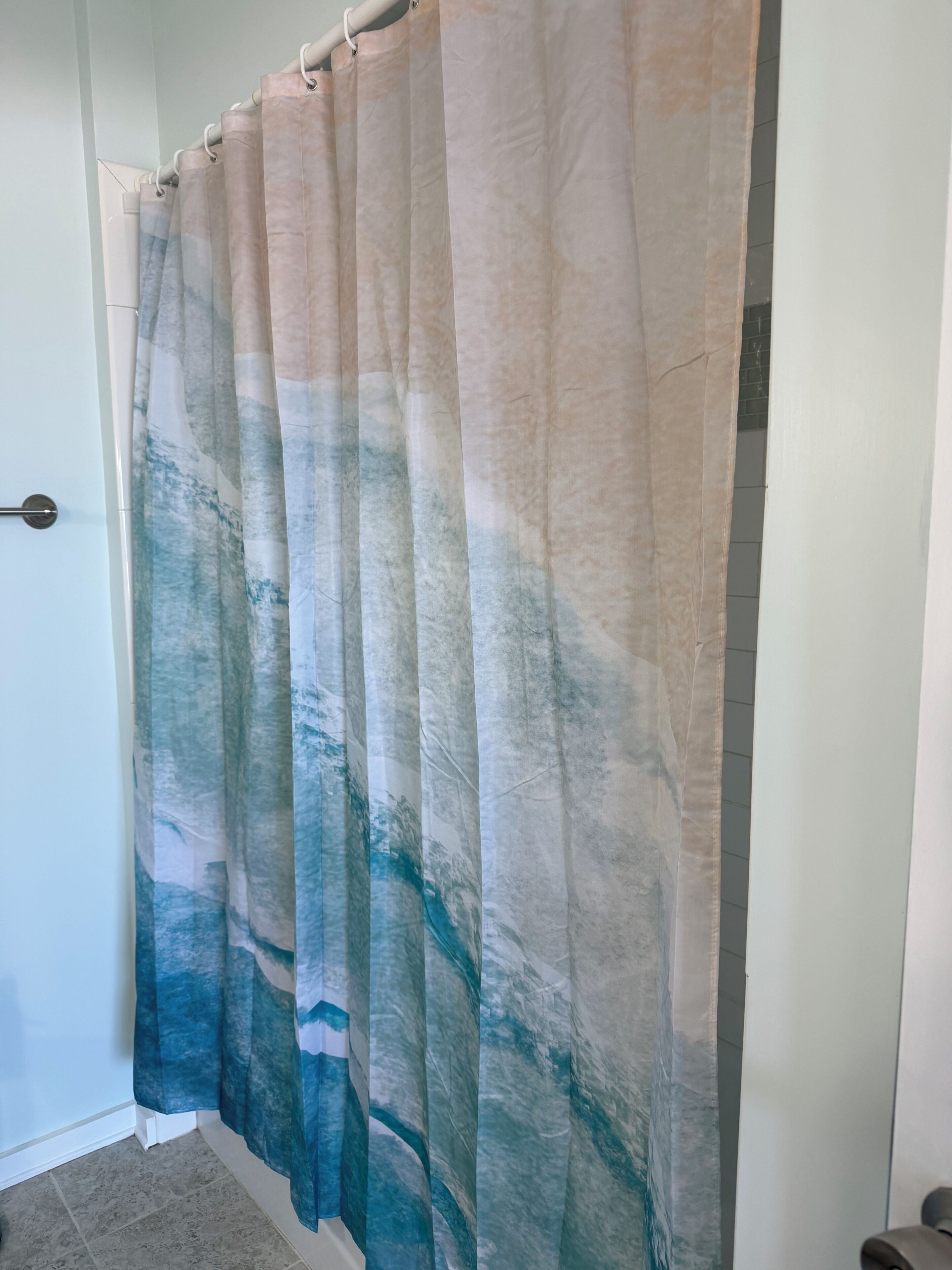A bathroom with a shower curtain featuring a blue and beige abstract pattern.