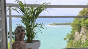 A statue of Buddha in a white pot on a balcony overlooking a coastal view with a lighthouse. - La Vue du Phare, Vue Mer Incroyable et Acces Privée Crique (Le Gosier)