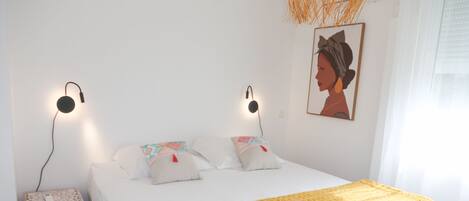 A neatly made bed with a yellow blanket, two bedside lamps, and a small bedside table with a phone.