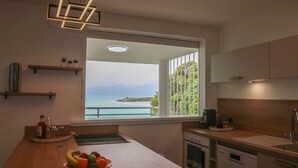 A modern kitchen with a view of the sea, a wooden countertop, and a bowl of fruit. - La Vue du Phare, Vue Mer Incroyable et Acces Privée Crique (Le Gosier)