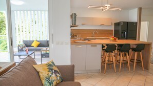 A modern kitchen with a central island, bar stools, and a dining area with a sofa and coffee table. - La Vue du Phare, Vue Mer Incroyable et Acces Privée Crique (Le Gosier)