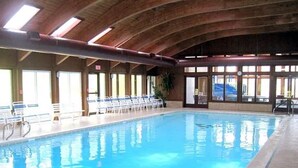 An indoor swimming pool with a wooden ceiling, clear windows, and sunlit areas.