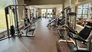 A gym with various exercise machines, large windows, and a high ceiling.