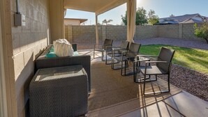 Un patio techado con mobiliario de mimbre, ventilador de techo y vista a un jardín trasero.