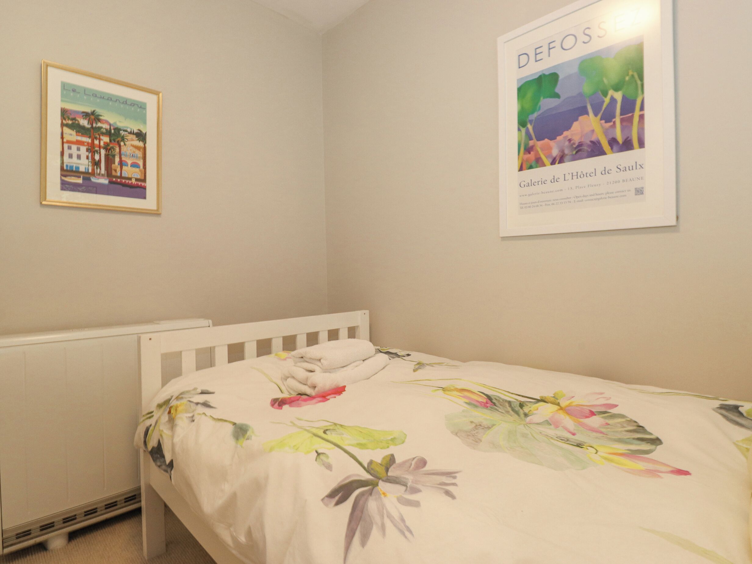 A bedroom with a single bed, a radiator, and two framed pictures on the wall.