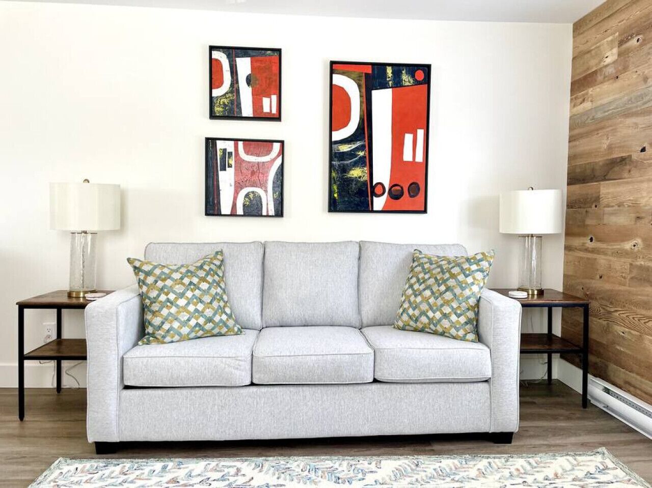Een woonkamer met een grijze bank, gekleurde kussens, abstracte wandkunst en een houten accentmuur.