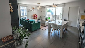 A modern kitchen with a dining area, a green sofa, and potted plants. - Bright Apartment Near the lake (Bordeaux)