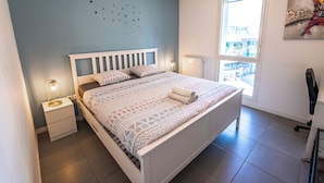 A neatly arranged bedroom with a bed, bedside lamps, a nightstand, a window with a view, and a wall-mounted artwork. - Bright Apartment Near the lake (Bordeaux)