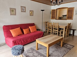 Una sala de estar acogedora con un sofá rojo, una mesa de comedor de madera y sillas. Hay cuadros en la pared y una lámpara de pie.