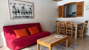 Una sala de estar con un sofá rojo, una mesa de centro de madera y una zona de comedor con sillas y una mesa de madera.