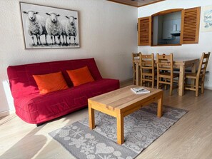 A living room with a red sofa, a wooden coffee table, and a dining area with wooden chairs and a table. - Sunny balcony, steps from the slopes (La Salle-les-Alpes)