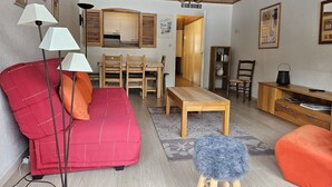 Una sala de estar acogedora con un sofá rojo, una mesa de comedor de madera y un taburete pequeño.
