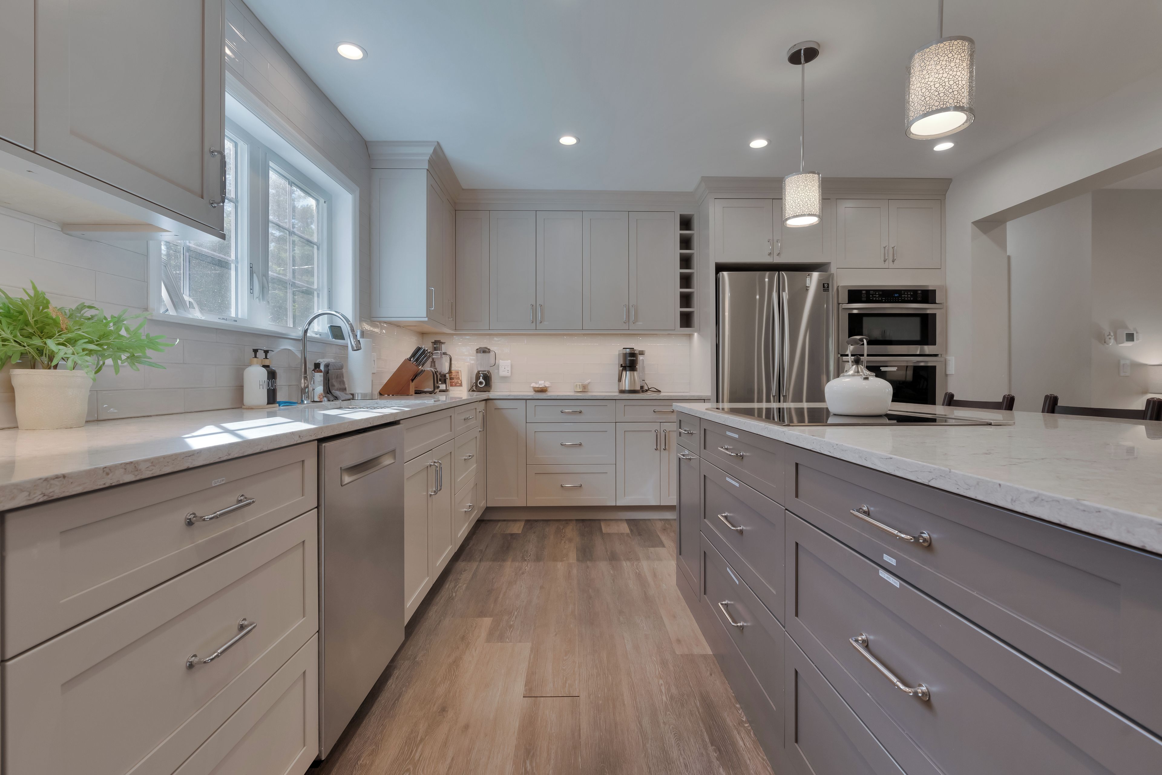 Une cuisine moderne dotée d’appareils électroménagers en acier inoxydable, de meubles de rangement gris et d’un plancher en bois.