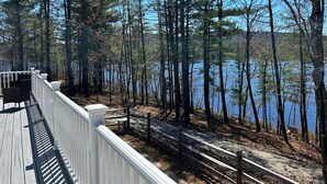 A deck with a white railing overlooking a lake surrounded by tall trees.