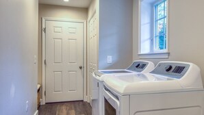 A laundry room with two front-loading washing machines, a door, and a window.