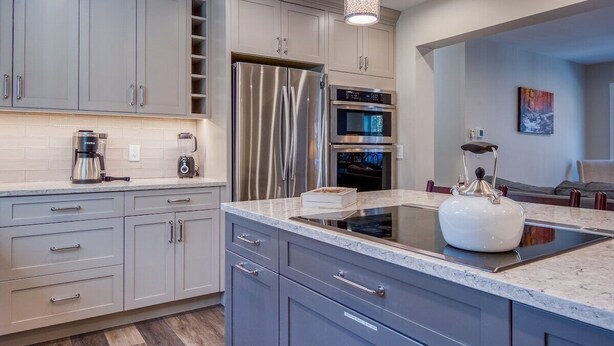 A modern kitchen with grey cabinets, stainless steel appliances, and a marble countertop.