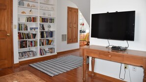 Ein Zimmer mit Holzboden, Bücherregal, Flachbildfernseher und Schreibtisch aus Holz.