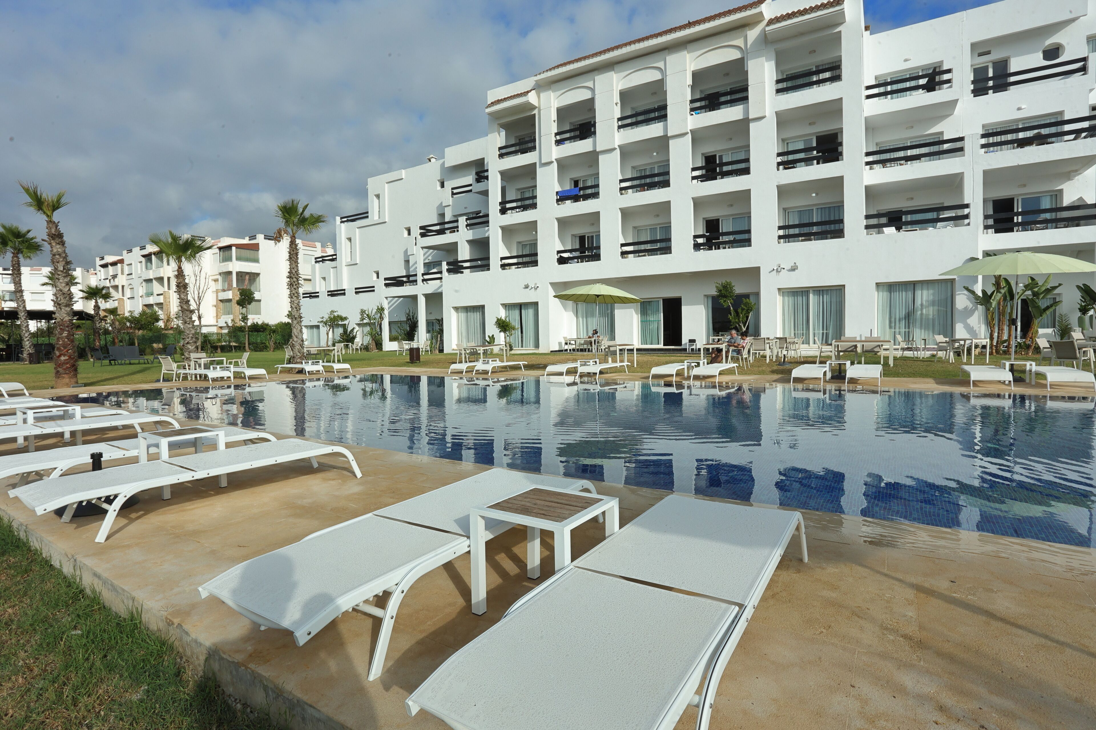 A hotel with a swimming pool, sun loungers, and a building with balconies.