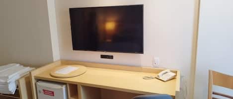 A small office space with a desk, chair, refrigerator, and a mounted television.