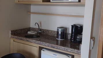 Una kitchenette compacta con microondas, cafetera y refrigerador pequeño.