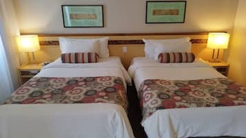 Habitación de hotel con dos camas individuales, cada una con colcha y almohadas estampadas, flanqueadas por mesitas de noche con lámparas.