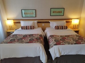 Une chambre d’hôtel avec deux lits simples, chacun agrémenté d’une couvre-lit et de coussins à motifs, et flanquée de deux tables de chevet avec des lampes.
