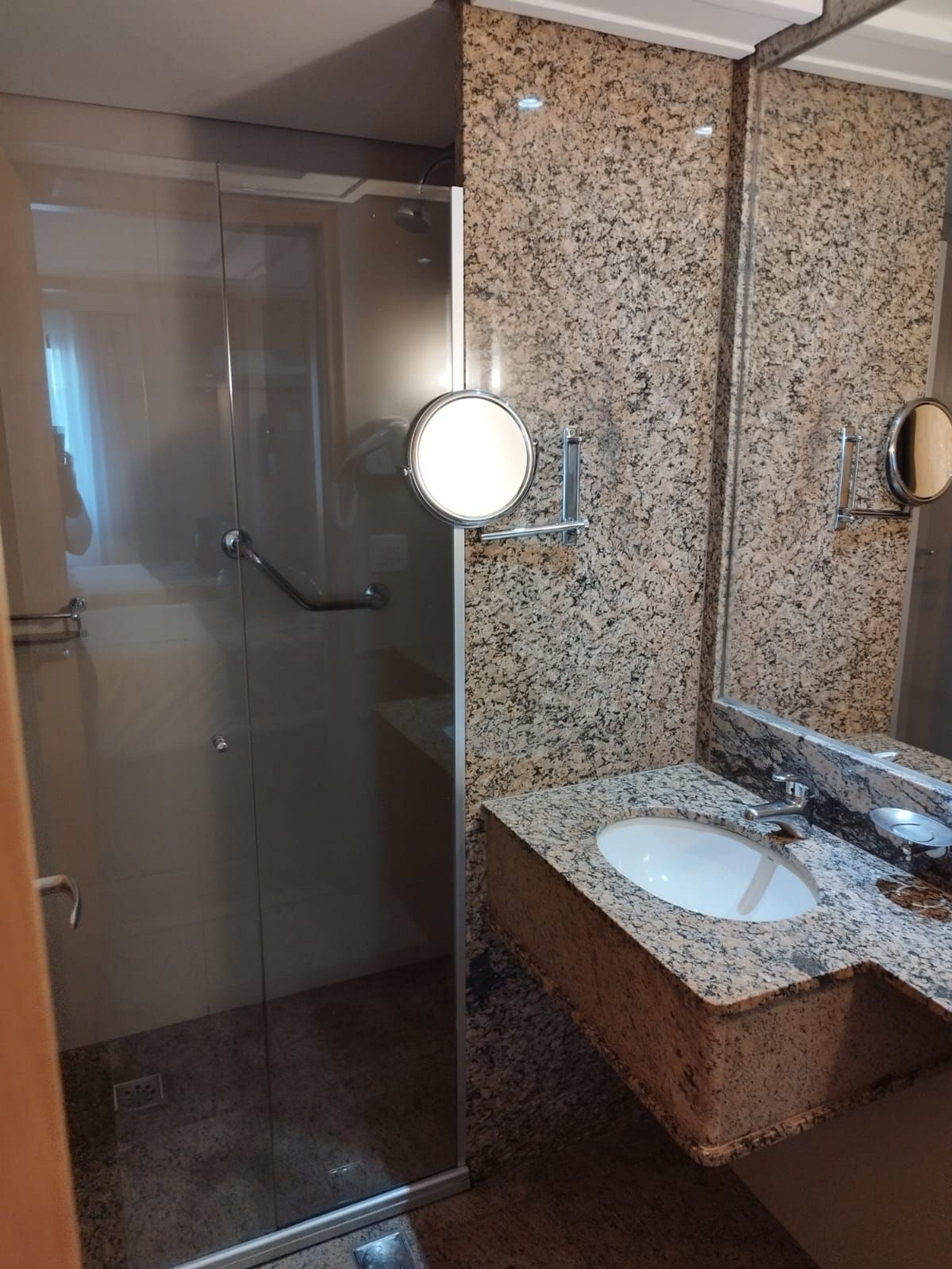 Ein Badezimmer mit Duschkabine aus Glas, Granit-Arbeitsplatten, einem Waschbecken und einem Spiegel.
