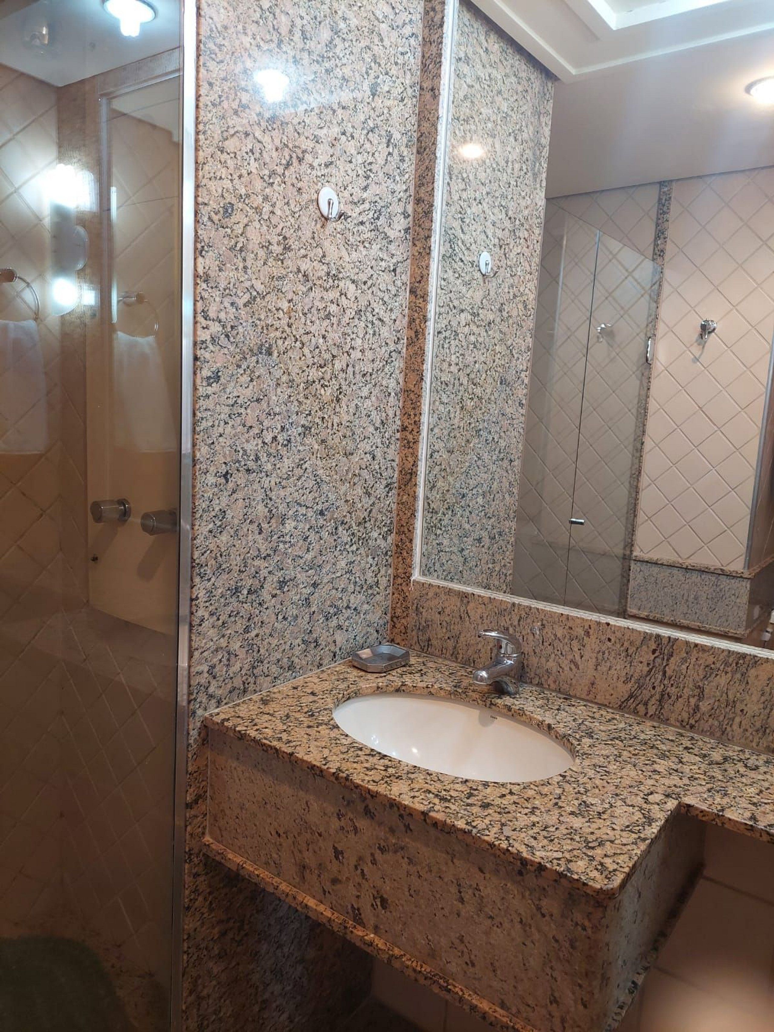 A bathroom with a granite countertop, a sink, a mirror, and a shower area.