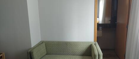 A small, green armchair in a corner of a room with a patterned bedspread.