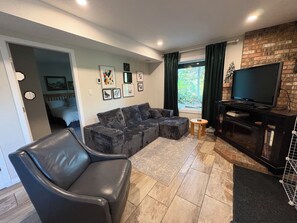 Una sala de estar con un sofá modular, un sillón de cuero, un televisor de pantalla plana y una chimenea.
