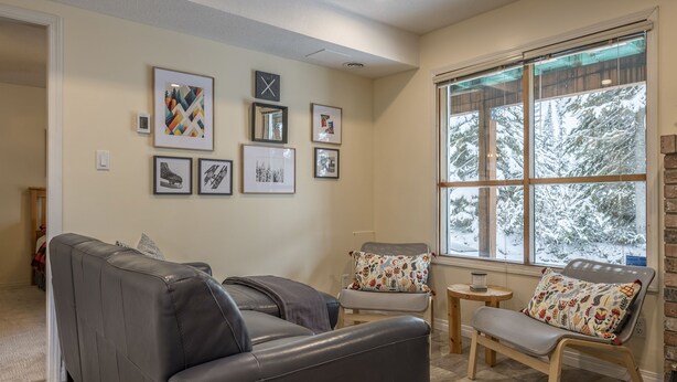 Un salon comprenant un canapé, un fauteuil, une petite table et une fenêtre donnant sur des arbres couverts de neige.