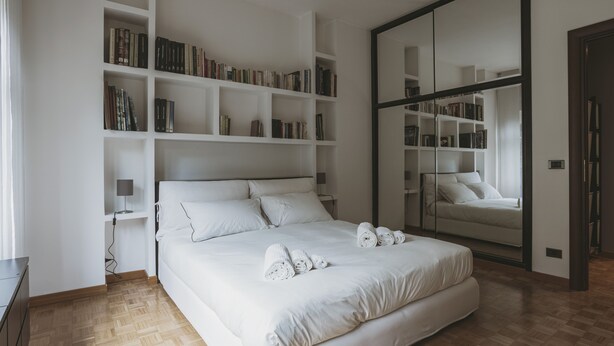 A modern bedroom with a large bed, white bedding, a bookshelf, and a mirrored closet. - San Pietro Cozy And Quiet Three-room Apt (Rome)