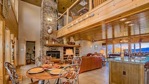 A spacious living area with a stone fireplace, wooden ceiling, and a large dining table with chairs.