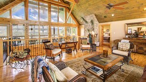 A spacious living area with high ceilings, large windows, and wooden furniture.