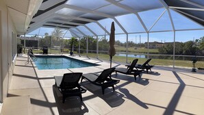 A covered outdoor area with a pool, lounge chairs, and a view of a lake and buildings. - Serenity now, full refund*, pool heat, sleeps 8 (Rotonda West)