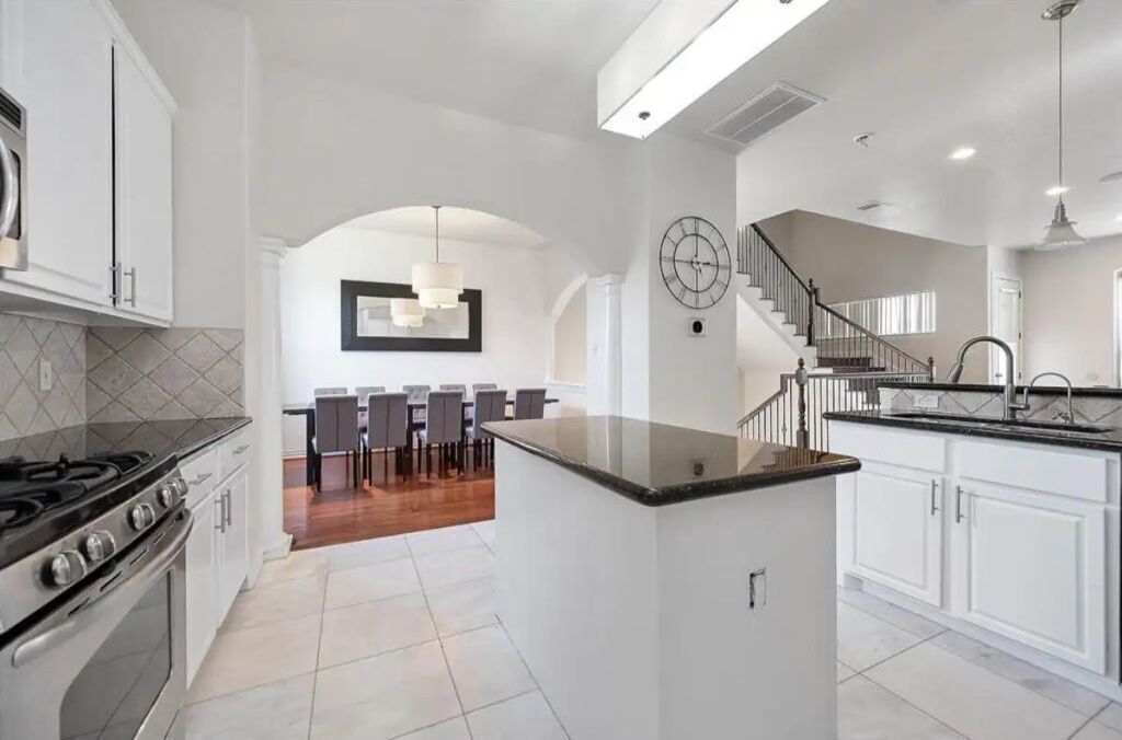 A modern kitchen with white cabinetry, a central island, and a dining area with chairs and a table.