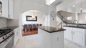 A modern kitchen with white cabinetry, a central island, and a dining area with chairs and a table. - Midtown Houston City View Home (Houston)