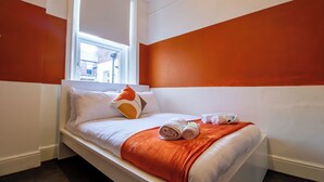 Une chambre d’hôtel avec un lit, du linge de lit blanc, un plaid rouge et une fenêtre donnant sur des immeubles.