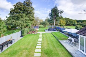 A backyard with a grassy lawn, a stone pathway, a covered seating area, and a fenced garden.