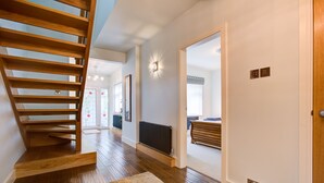 A modern interior with a wooden staircase, a radiator, and a hallway leading to another room.