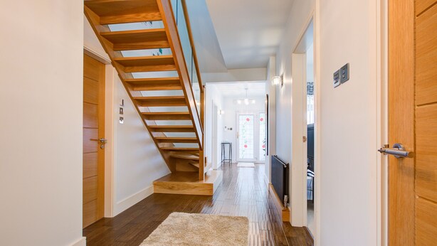 A modern hallway with a wooden staircase, a white carpet, and a door leading to a room with a radiator.