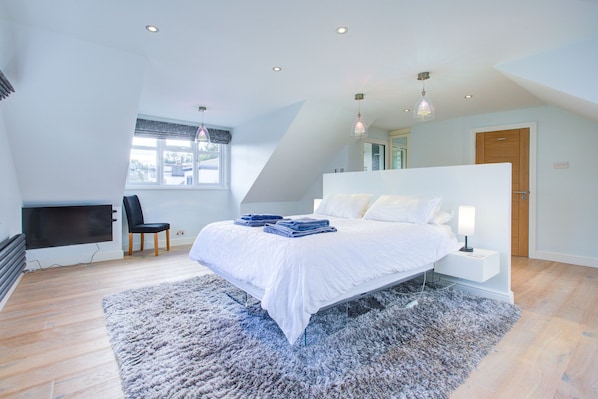 A modern bedroom with a large bed, a desk, and a chair.